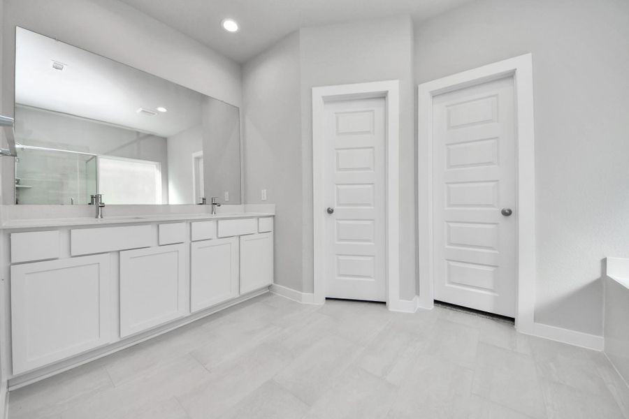 Escape to a spa-like oasis in this primary bathroom. Enjoy a walk-in shower with tile surround, a separate garden tub with custom detailing, and an elegant vanity featuring light countertops, modern hardware, and beautiful vanity lights. Experience luxury and relaxation in every detail. Sample photo of completed home with similar floor plan. Actual colors and selections may vary. Escape to a spa-like oasis in this primary bathroom. Enjoy a walk-in shower with tile surround, a separate garden tub with custom detailing, and an elegant vanity featuring light countertops, modern hardware, and beautiful vanity lights. Experience luxury and relaxation in every detail. Sample photo of completed home with similar floor plan. Actual colors and selections may vary.