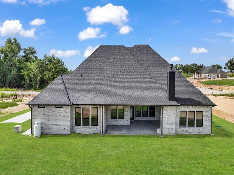 Back of property featuring a patio area, a shingled roof, a lawn, and brick siding Back of property featuring a patio area, a shingled roof, a lawn, and brick siding