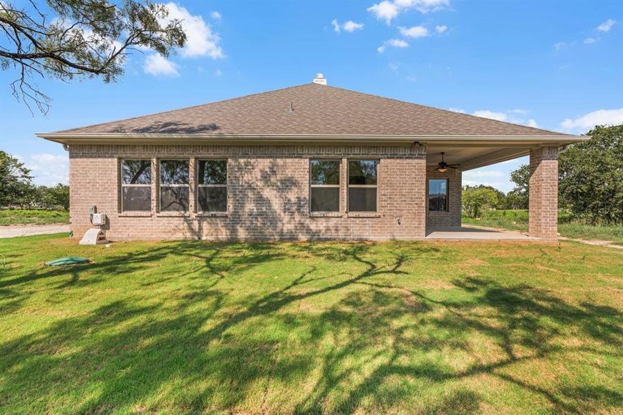 Back of property featuring brick siding, a yard, a patio area, a shingled roof, and a ceiling fan