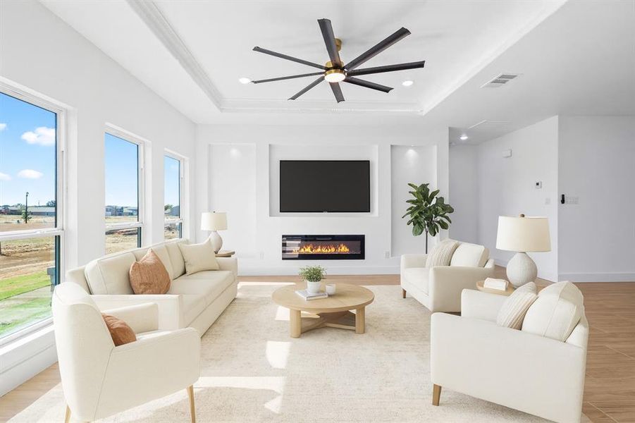 Living area with a glass covered fireplace, a raised ceiling, a ceiling fan, light wood-style floors, and recessed lighting Living area with a glass covered fireplace, a raised ceiling, a ceiling fan, light wood-style floors, and recessed lighting