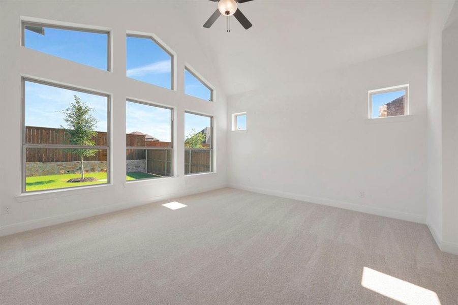 Vaulted ceiling room featuring a multi-pane window wall, light-toned carpet, a ceiling fan, and two high wall windows Vaulted ceiling room featuring a multi-pane window wall, light-toned carpet, a ceiling fan, and two high wall windows
