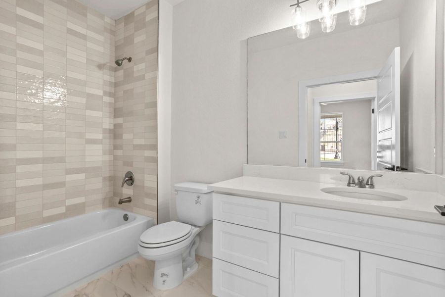Bathroom featuring a white bathtub with a tiled surround, a white toilet, and a vanity with a white countertop and integrated sink Bathroom featuring a white bathtub with a tiled surround, a white toilet, and a vanity with a white countertop and integrated sink