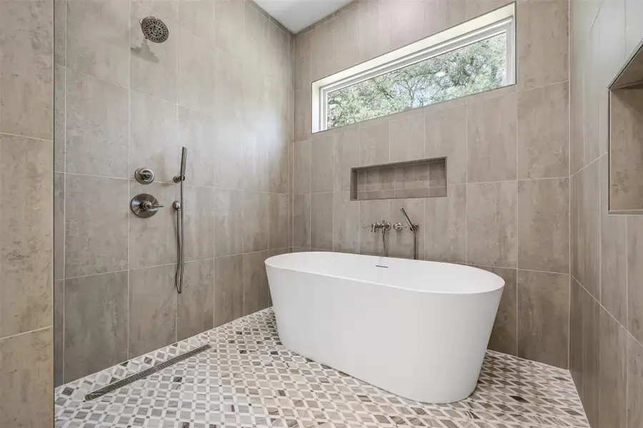 Bathroom featuring a soaking tub, tiled shower, and tile walls