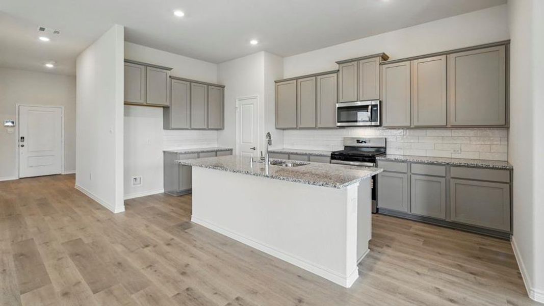 Kitchen featuring gray cabinetry, light stone countertops, an island with sink, stainless steel appliances, and light wood finished floors