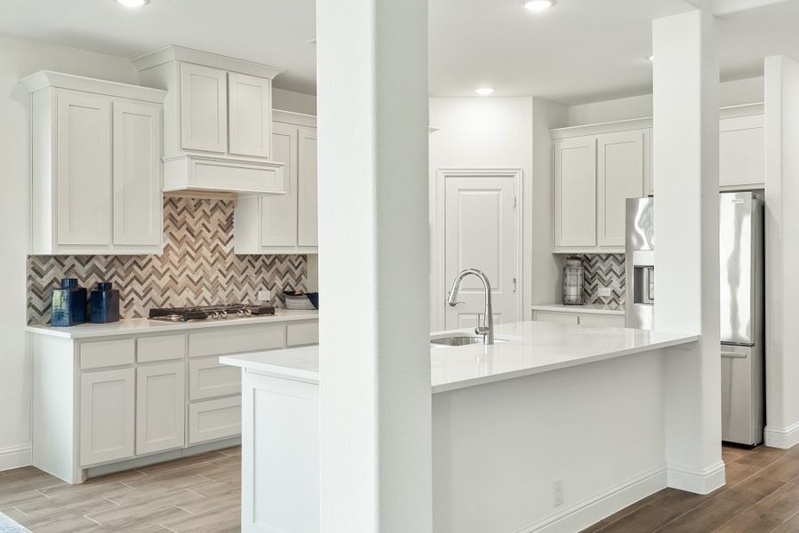Kitchen with white cabinets, chevron tile backsplash, center island with sink, and stainless steel refrigerator