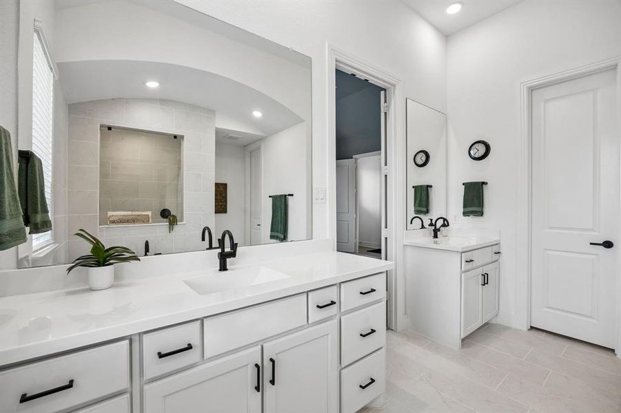 Dual vanity bathroom featuring white cabinetry with black hardware, white countertops, and light-toned tile flooring Dual vanity bathroom featuring white cabinetry with black hardware, white countertops, and light-toned tile flooring