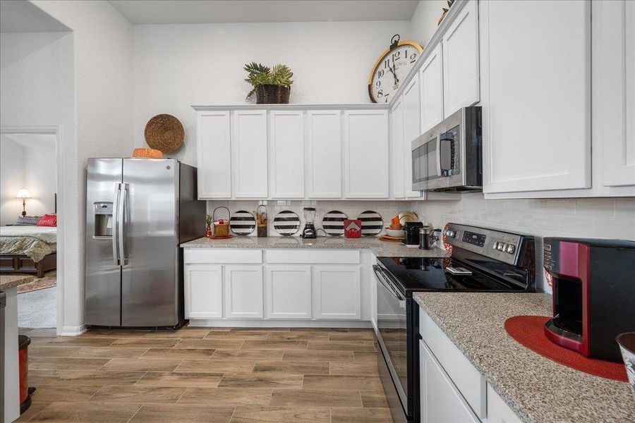 Kitchen featuring appliances with stainless steel finishes, white cabinetry, light stone counters, decorative backsplash, and wood finish floors Kitchen featuring appliances with stainless steel finishes, white cabinetry, light stone counters, decorative backsplash, and wood finish floors