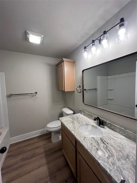 Full bathroom featuring toilet, a washtub, baseboards, wood finished floors, and vanity