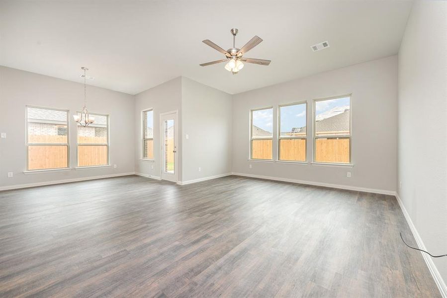 Spare room with ceiling fan with notable chandelier, a healthy amount of sunlight, and dark hardwood / wood-style floors