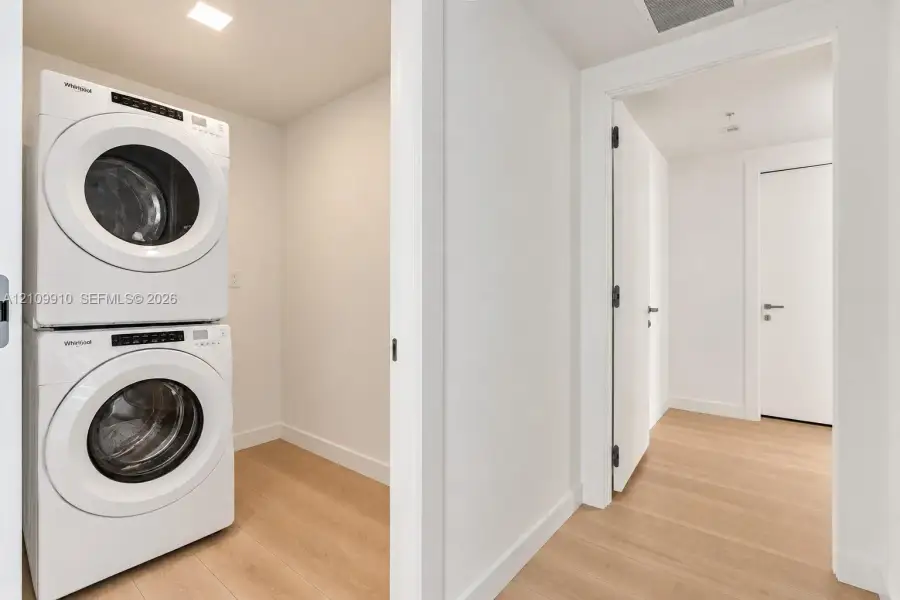 Utility space featuring a stacked white laundry unit, recessed ceiling lighting, and wood-finish flooring