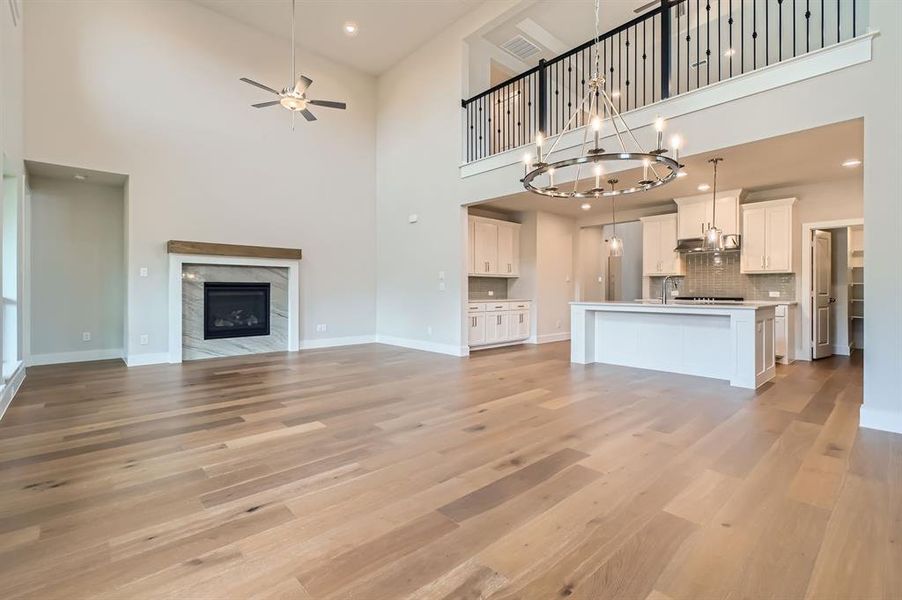 Unfurnished living room featuring a towering ceiling, ceiling fan, light wood-style floors, a fireplace, and a chandelier Unfurnished living room featuring a towering ceiling, ceiling fan, light wood-style floors, a fireplace, and a chandelier