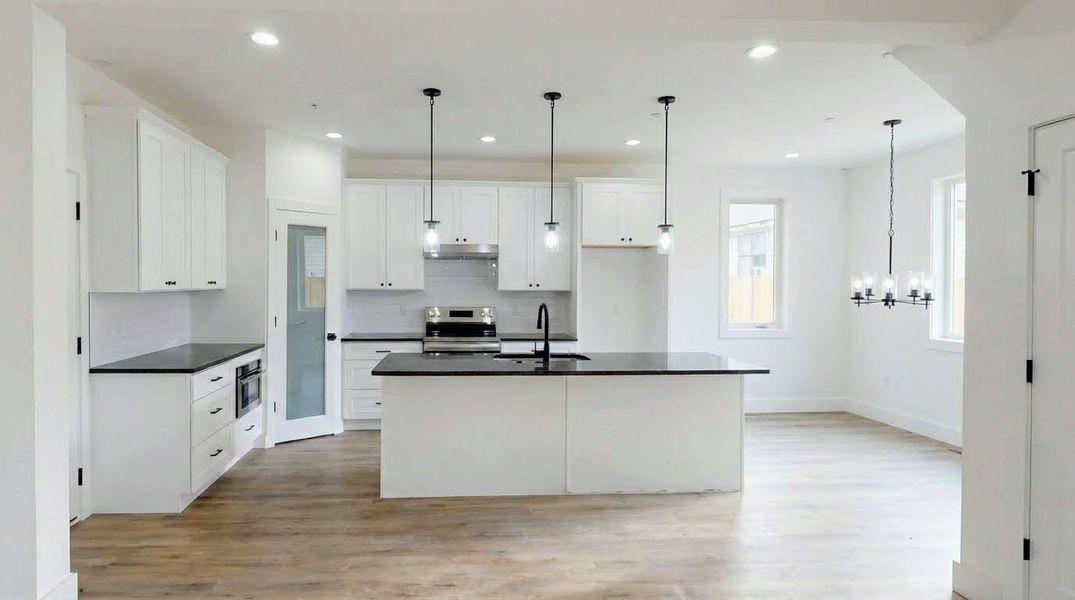 Kitchen featuring light wood-style flooring, a kitchen island with sink, white cabinetry, stainless steel appliances, and a chandelier