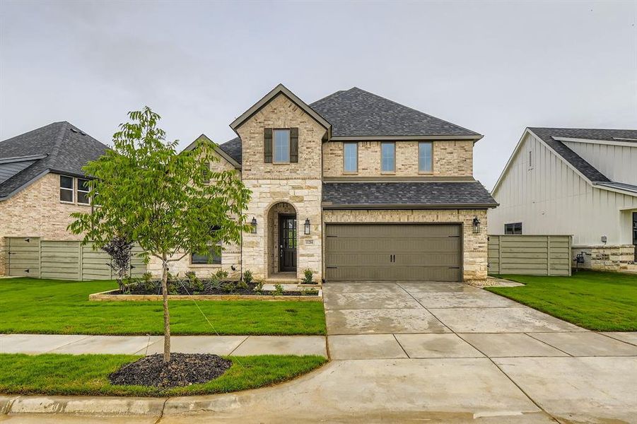 French country inspired facade featuring a shingled roof, an attached garage, concrete driveway, brick siding, and stone siding French country inspired facade featuring a shingled roof, an attached garage, concrete driveway, brick siding, and stone siding