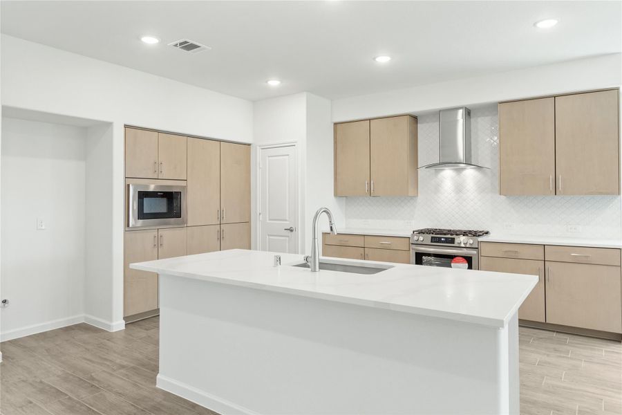 Modern kitchen with large white island, tan cabinets, stainless steel range, hood vent, and built-in microwave