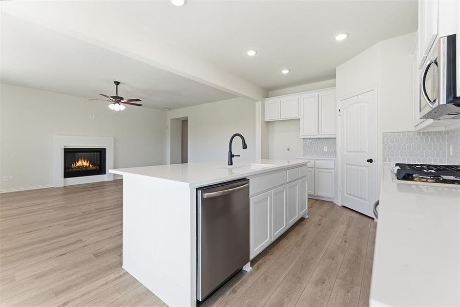 Kitchen with light stone counters, stainless steel appliances, recessed lighting, a glass covered fireplace, and white cabinetry