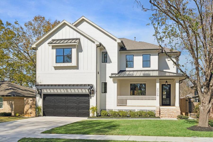 A striking modern farmhouse exterior blends timeless charm with contemporary sophistication. This two-story home showcases pristine white siding accented by sleek black-framed windows and a bold garage door. A charming covered front porch with a standing seam metal roof and brick steps invites you inside, while a pergola detail adds dimension and character to the garage. Thoughtful landscaping frames the front yard, and the expansive driveway provides ample parking.