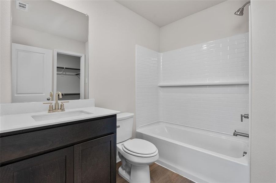 Bathroom featuring shower combination, vanity, dark wood-style flooring, and a spacious closet Bathroom featuring shower combination, vanity, dark wood-style flooring, and a spacious closet