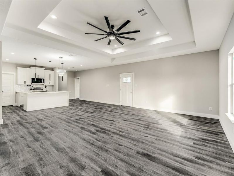 Unfurnished living room featuring ceiling fan, dark hardwood / wood-style flooring, and a raised ceiling