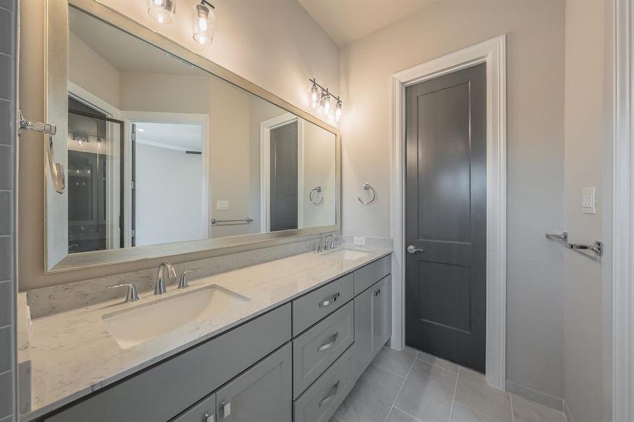 Bathroom featuring a double vanity with grey cabinetry, dual undermount sinks, and a light-toned countertop