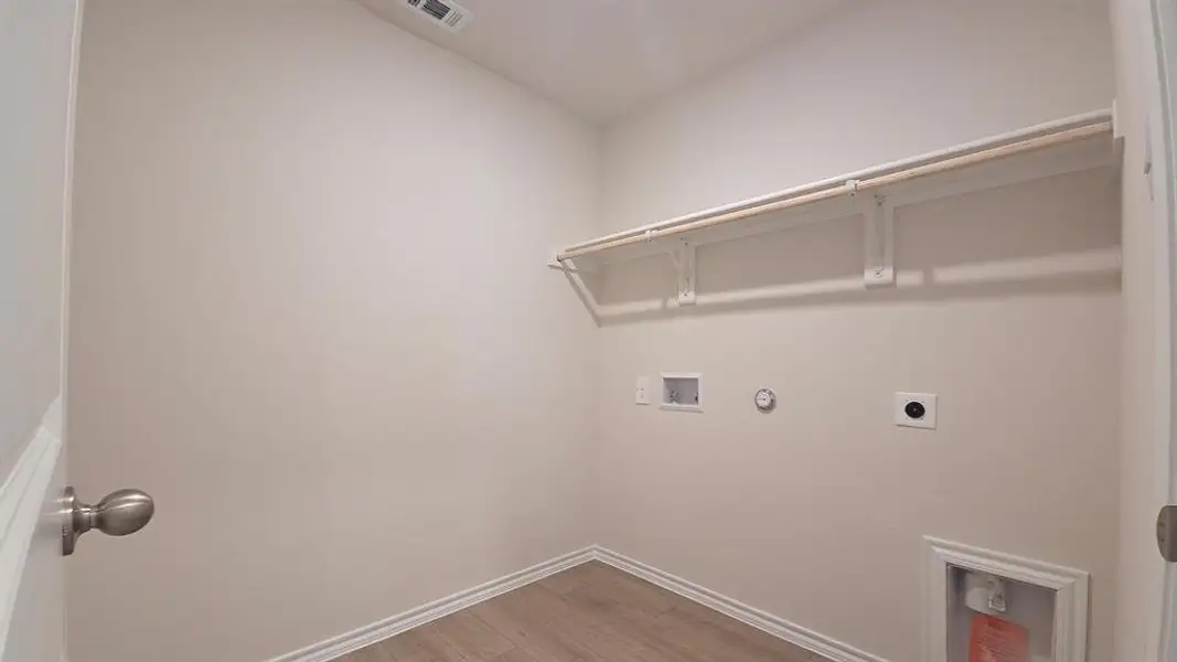Dedicated laundry area featuring wood-finish flooring, light-toned walls, and a built-in shelf with hanging rod