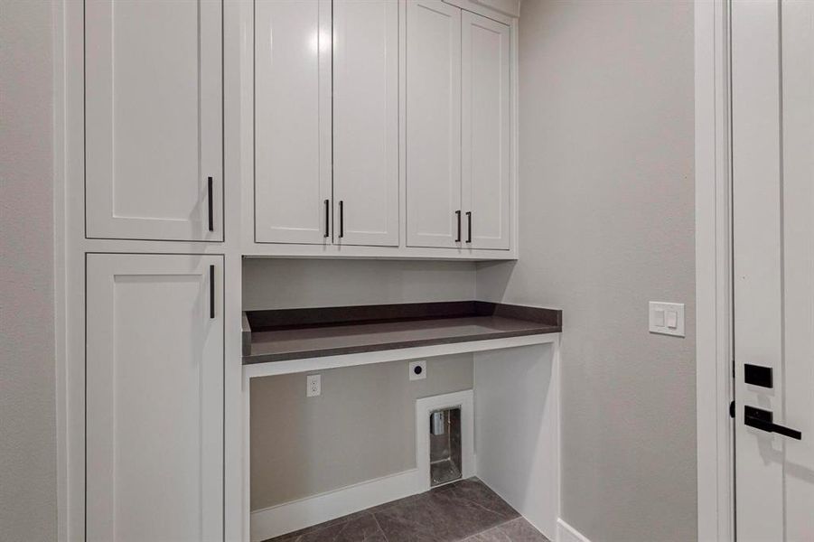 Clothes washing area with cabinets, dark tile patterned flooring, and electric dryer hookup