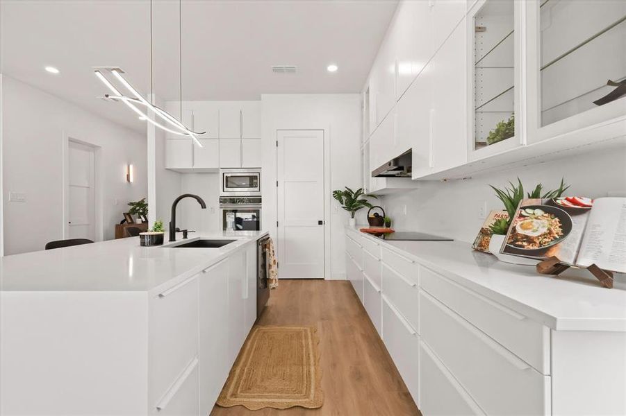 Kitchen with modern cabinets, white cabinetry, light wood-style floors, a center island with sink, and glass insert cabinets Kitchen with modern cabinets, white cabinetry, light wood-style floors, a center island with sink, and glass insert cabinets