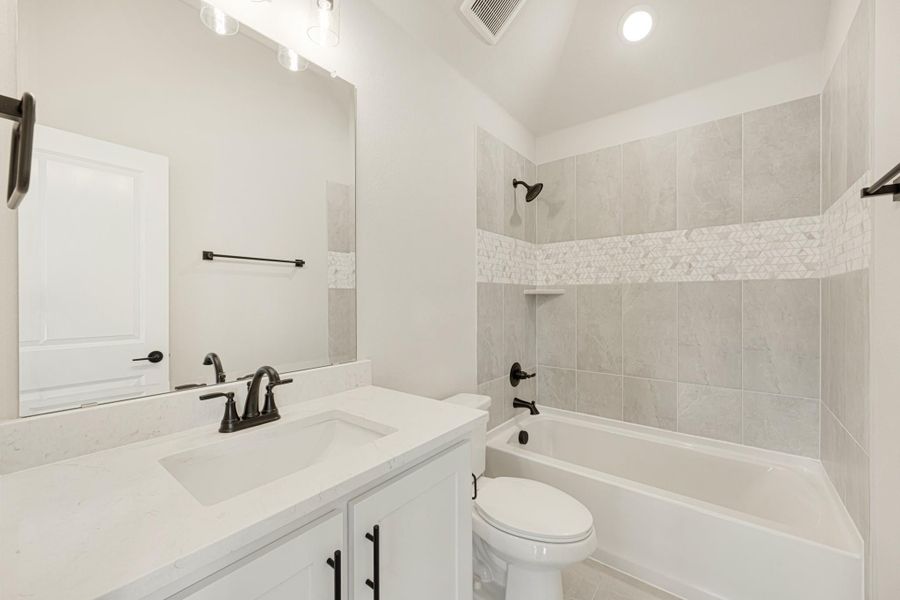 Bathroom with white vanity, quartz countertop, tub-shower combo with gray tile surround, and dark bronze fixtures