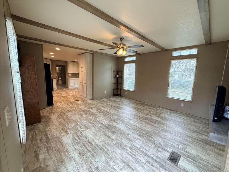 Unfurnished living room with a ceiling fan, beamed ceiling, and light wood-style flooring