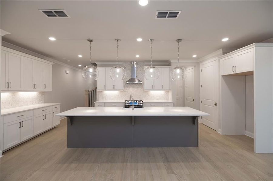 Kitchen featuring pendant lighting, a center island with sink, and wall chimney exhaust hood