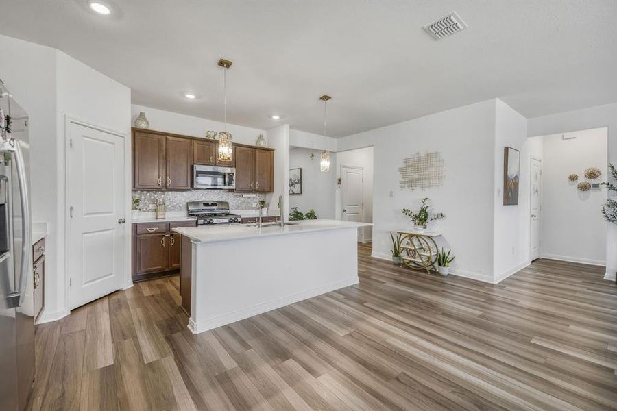 Kitchen featuring wood-finish flooring, white walls, dark wood cabinetry, stainless steel appliances, and a central island with a white countertop Kitchen featuring wood-finish flooring, white walls, dark wood cabinetry, stainless steel appliances, and a central island with a white countertop
