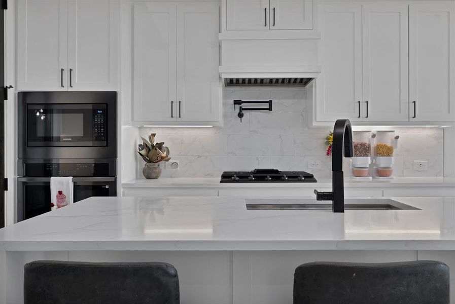 Kitchen featuring custom range hood, white cabinetry, stainless steel oven, black gas stovetop, and built in microwave