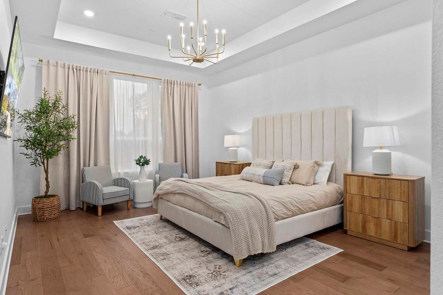 Bedroom with hardwood / wood-style floors, a raised ceiling, and a chandelier