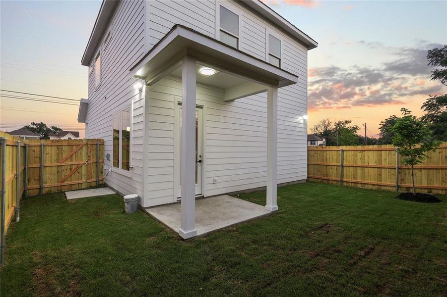 Back of house at dusk with a fenced backyard and a patio