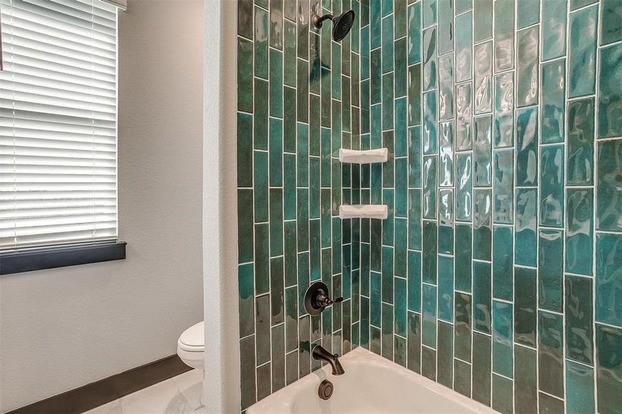 Bathroom with tiled shower / bath combo, a healthy amount of sunlight, and toilet