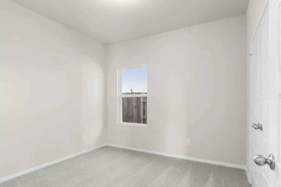 Image of a bedroom with cream walls. tan carpeting, white trim and a window