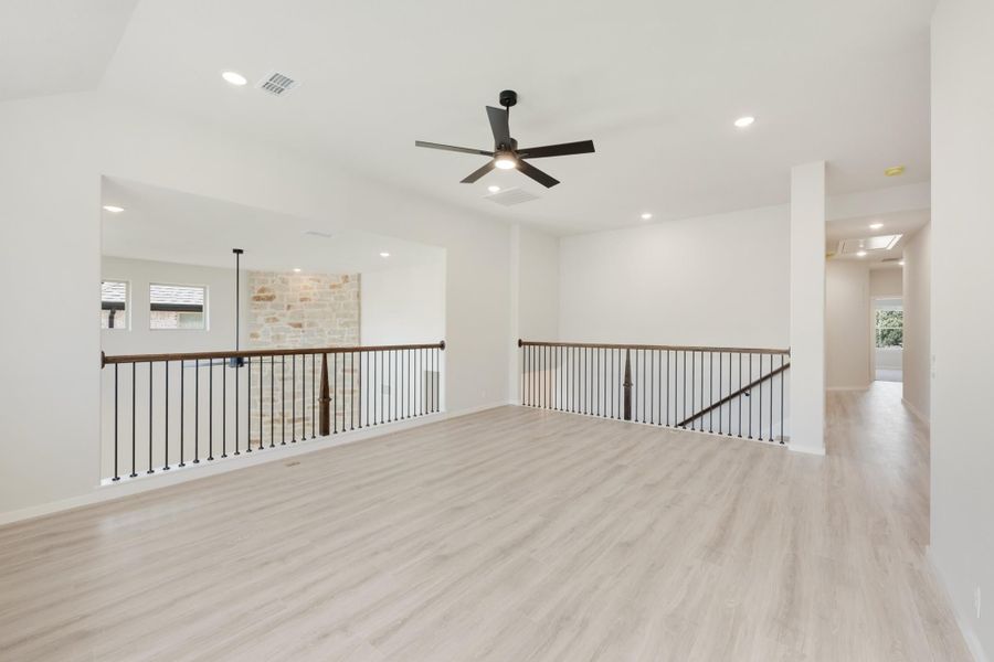 Open upstairs loft with light wood floors, black ceiling fan, and iron stair railings overlooking lower level