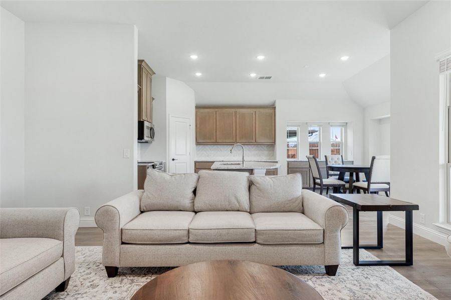 Open-concept living room with beige sofa, hardwood floors, and kitchen visible in background