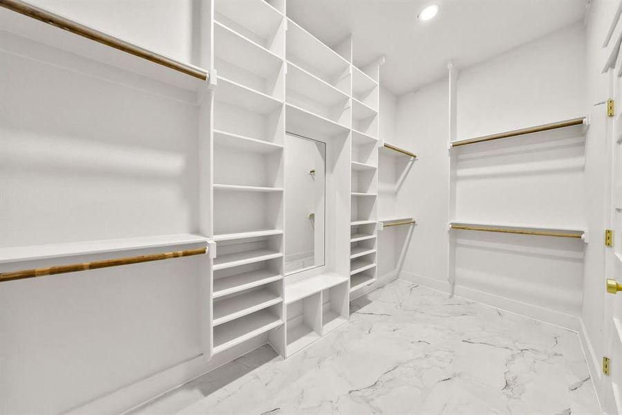 Spacious custom closet featuring white built-in shelving, multiple hanging rods, and a full-length mirror