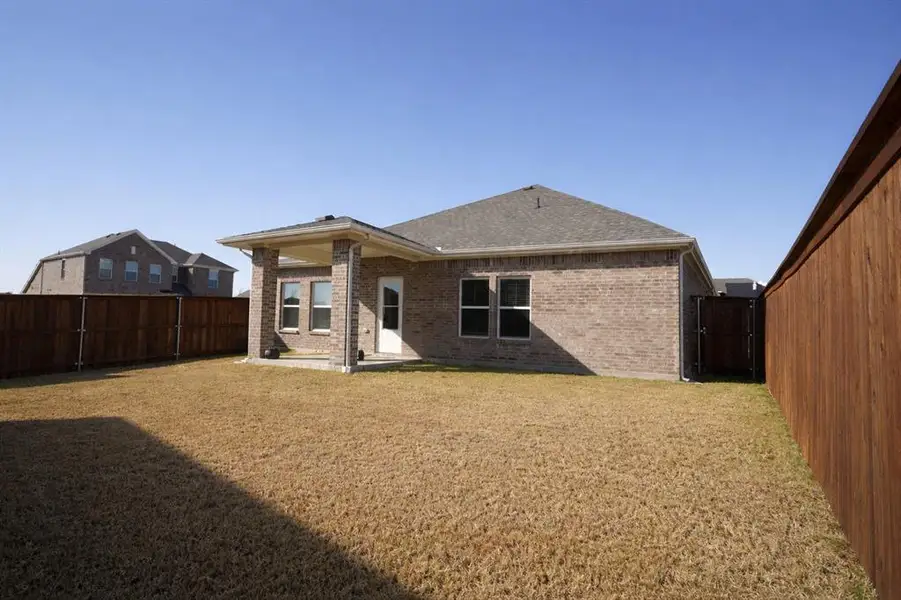 Back of house featuring brick siding, a patio, a fenced backyard, and roof with shingles