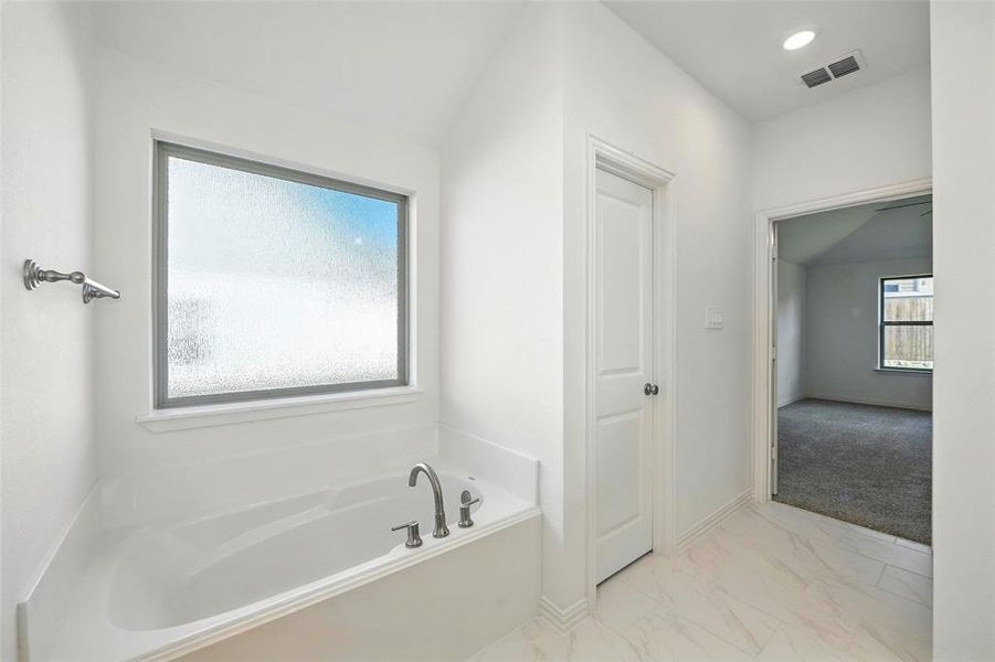 Bathroom featuring a garden tub and marble finish floors