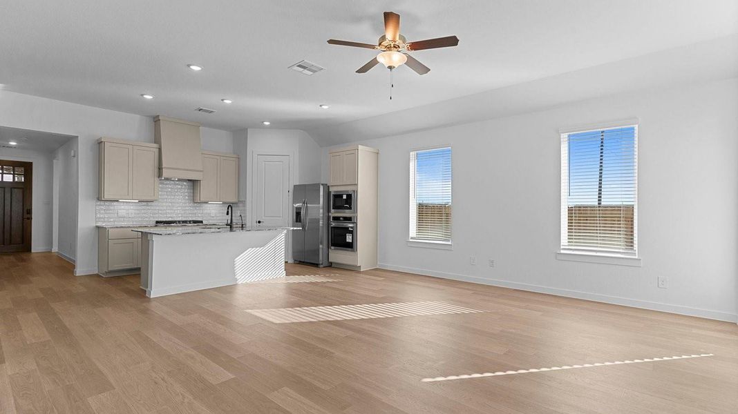 A cozy living room featuring large windows for natural lighting, vinyl wood flooring and a view to the kitchen and dining area.