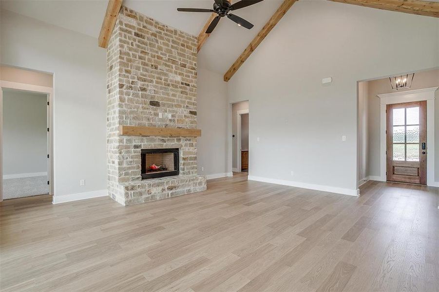 Unfurnished living room with beamed ceiling, high vaulted ceiling, light wood-type flooring, and ceiling fan with notable chandelier