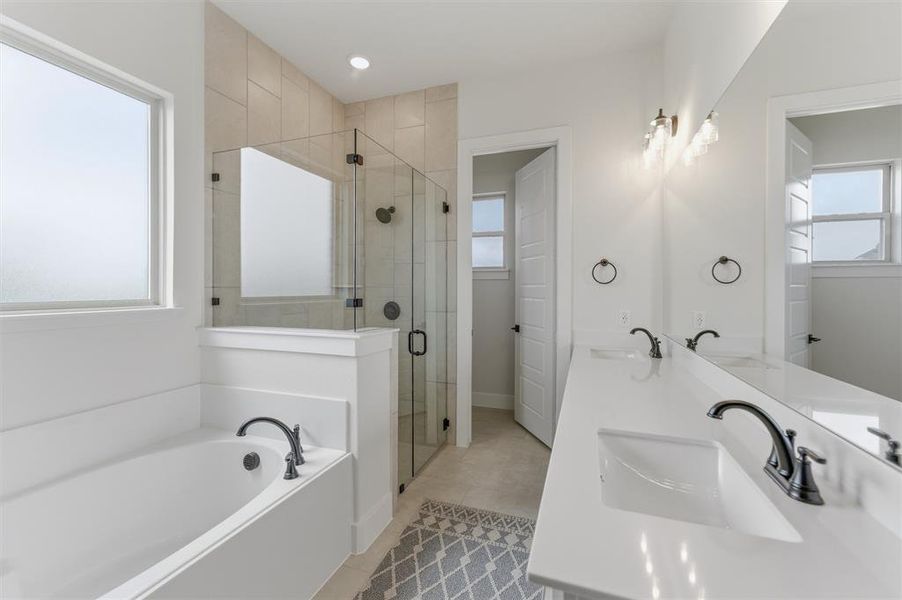 Bathroom featuring a built-in soaking tub with dark bronze fixtures, a glass-enclosed shower with tiled walls, dual vanity with undermount sinks and dark bronze faucets, and a large mirror with sconce lighting