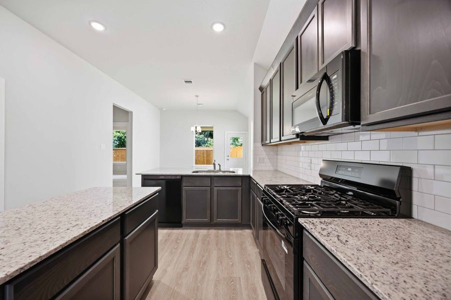Kitchen with dark cabinets, granite countertops, black appliances, and white subway tile backsplash Kitchen with dark cabinets, granite countertops, black appliances, and white subway tile backsplash