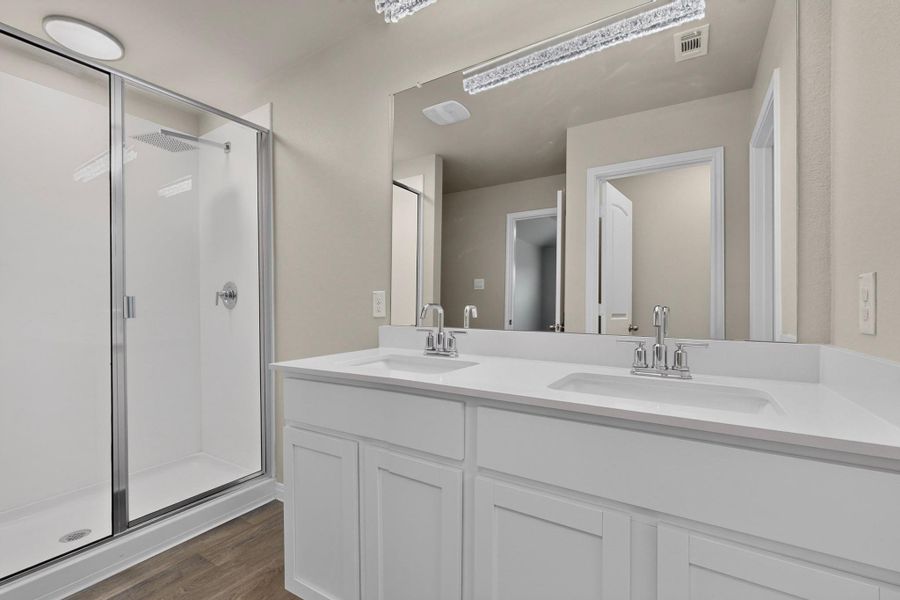 A modern double vanity stands adjacent to a glass-enclosed walk-in shower with wood-style flooring.
