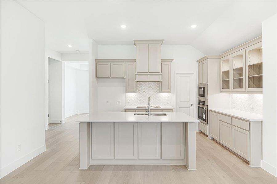 Kitchen with gray cabinets, center island with sink, tile backsplash, and light hardwood floors