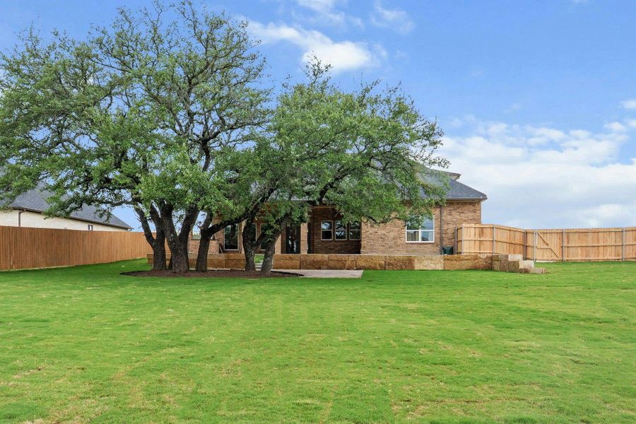 Expansive backyard featuring a lush lawn, mature trees, a brick and stone exterior, a private patio, and a wood privacy fence