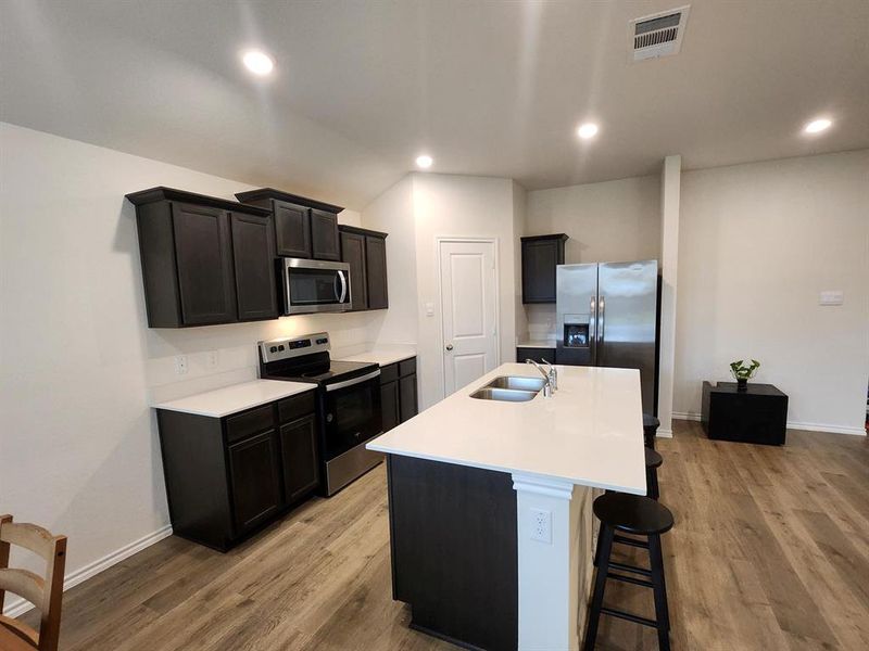 Kitchen featuring stove, a kitchen island with sink, a breakfast bar area, stainless steel fridge, and light wood-style floors