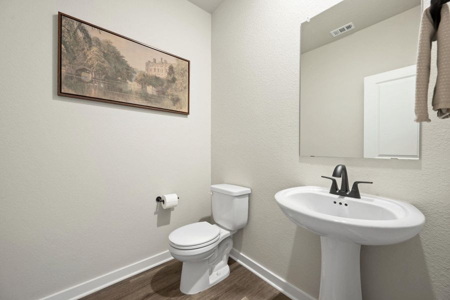 A classic pedestal sink pairs with warm wood-look flooring in this half bath. A classic pedestal sink pairs with warm wood-look flooring in this half bath.