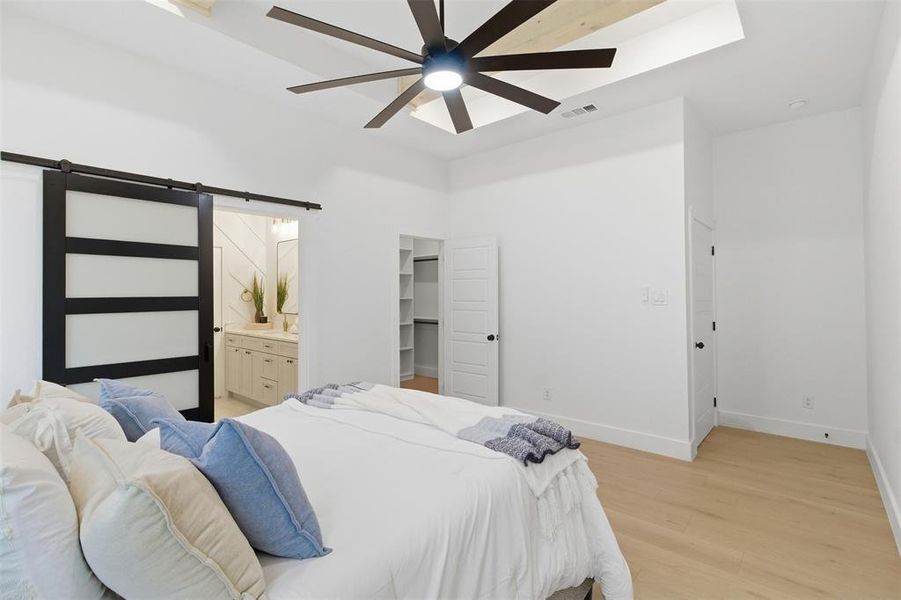 Spacious room featuring light wood-finish flooring, a tray ceiling with wood paneling, and a large ceiling fan with integrated lighting